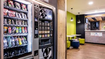 Ein Getränke- und Snackautomaten, eine Wand mit Holzverkleidung und eine Sitzecke mit gelben Stühlen.
