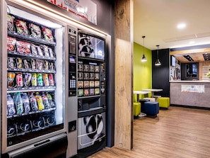 A vending machine with snacks and beverages, a wooden accent wall, and a seating area with yellow chairs.
