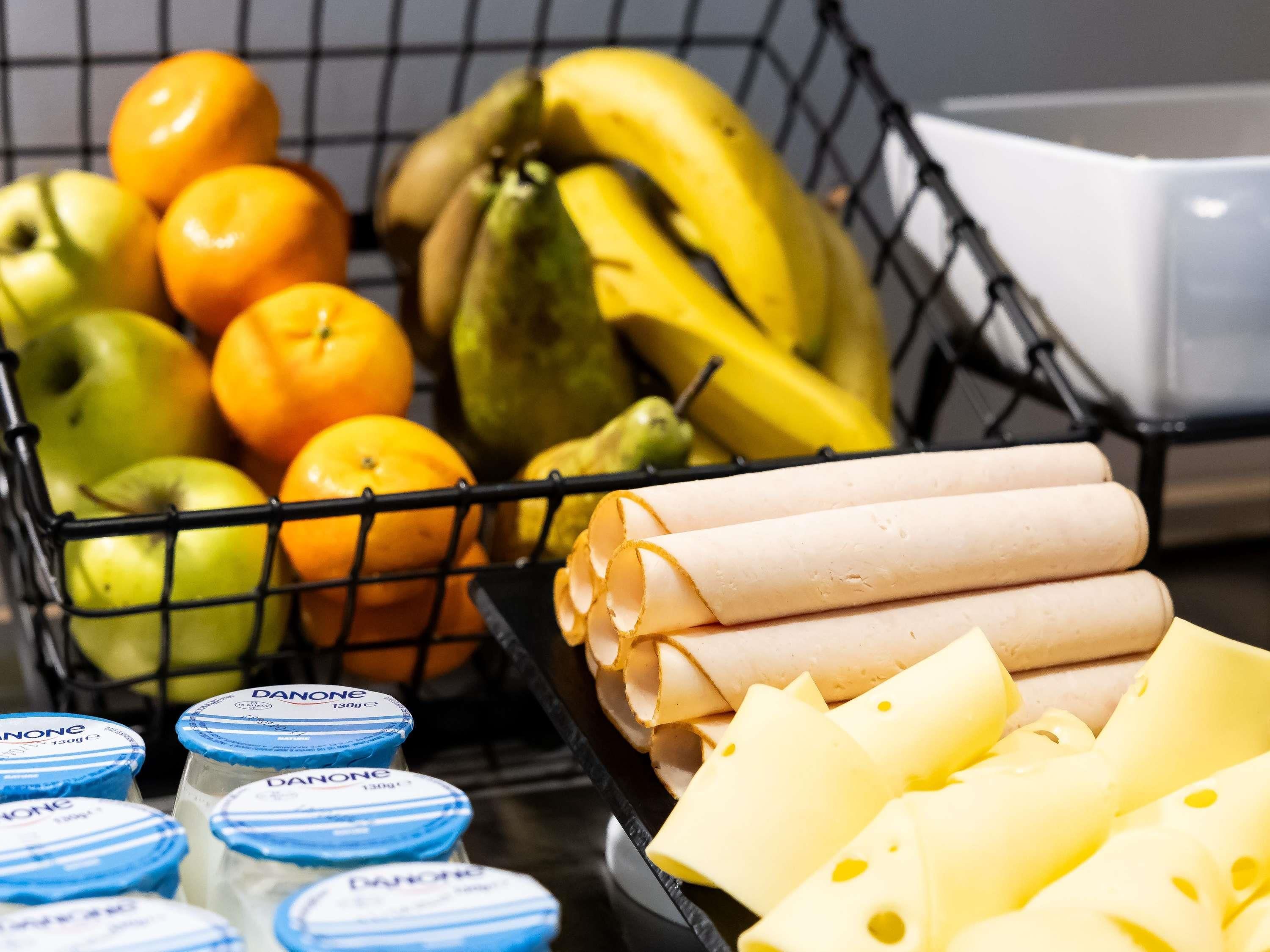 Una cesta de mimbre con frutas, queso y recipientes de yogur.