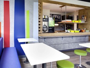 A modern cafe with white tables and green stools, a coffee machine, and a menu board. - ibis budget Clermont-Ferrand Nord Riom (Riom)