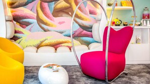 Une pièce moderne agrémentée d’une fresque murale abstraite aux couleurs vives, d’un fauteuil rouge, d’un pouf blanc et d’une chaise jaune.