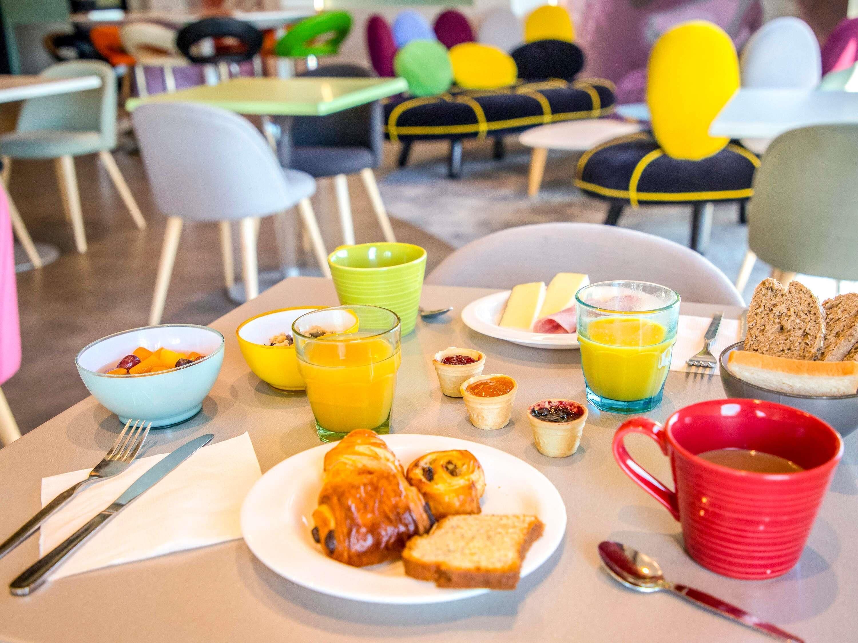 A breakfast setting with a plate of croissants, toast, and jam, accompanied by glasses of orange juice and a red mug.