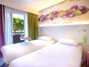 A hotel room with two beds, a window with curtains, a wall mural, a bedside table, and a green wall socket.
