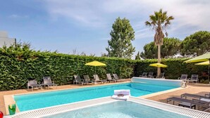 Une piscine entourée de verdure et d’arbres, avec des chaises longues et des parasols.