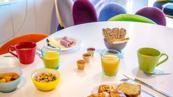 Una mesa de desayuno con diversos alimentos y bebidas, como cruasanes, pan y jugo.