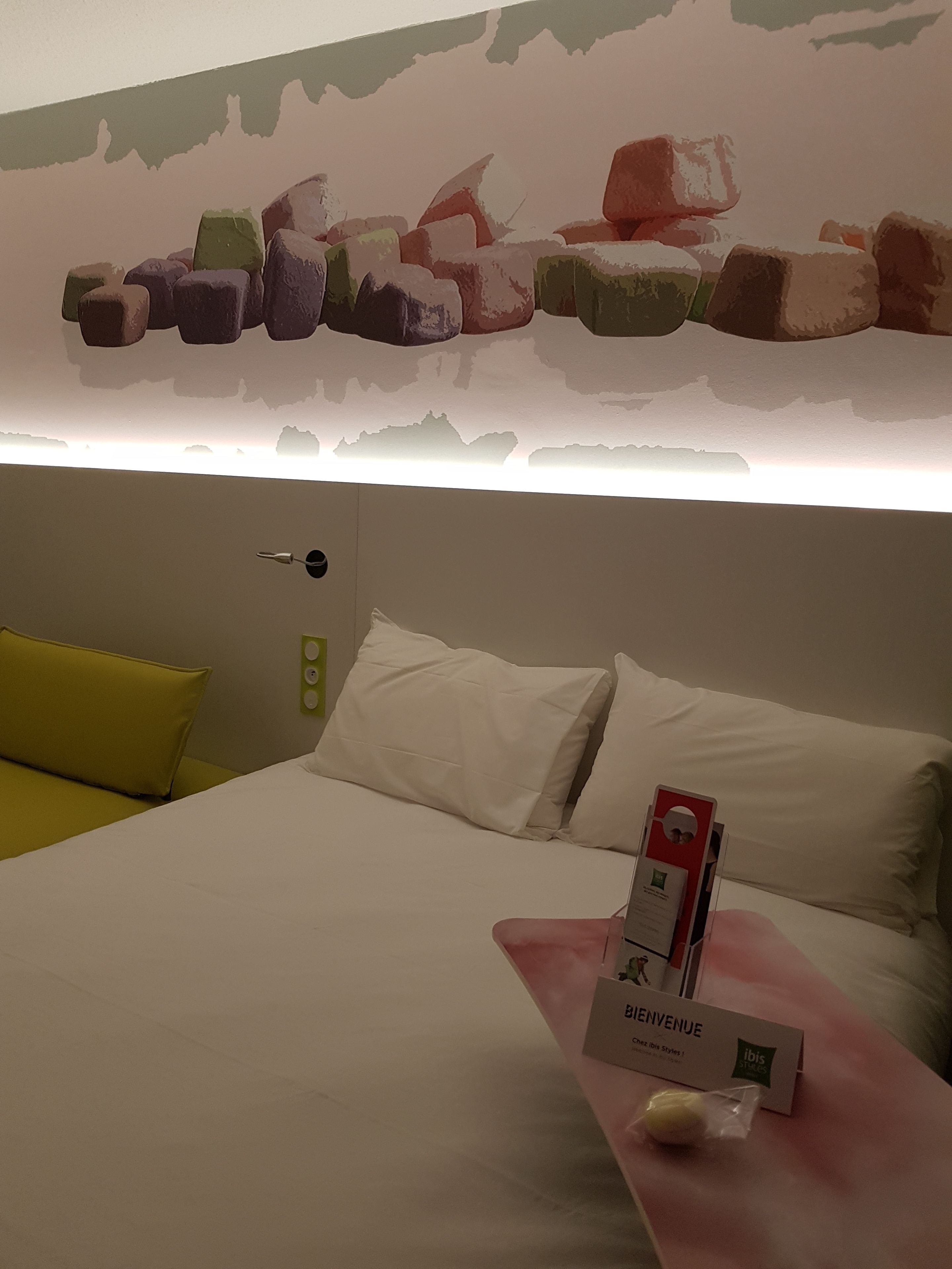 A hotel room with a bed, pillows, a bedside table with a tissue box, and a wall art piece above the bed.