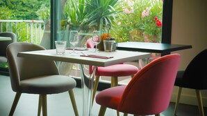 Un coin repas avec une table dressée pour deux personnes, des chaises et une vue sur la verdure à l’extérieur.