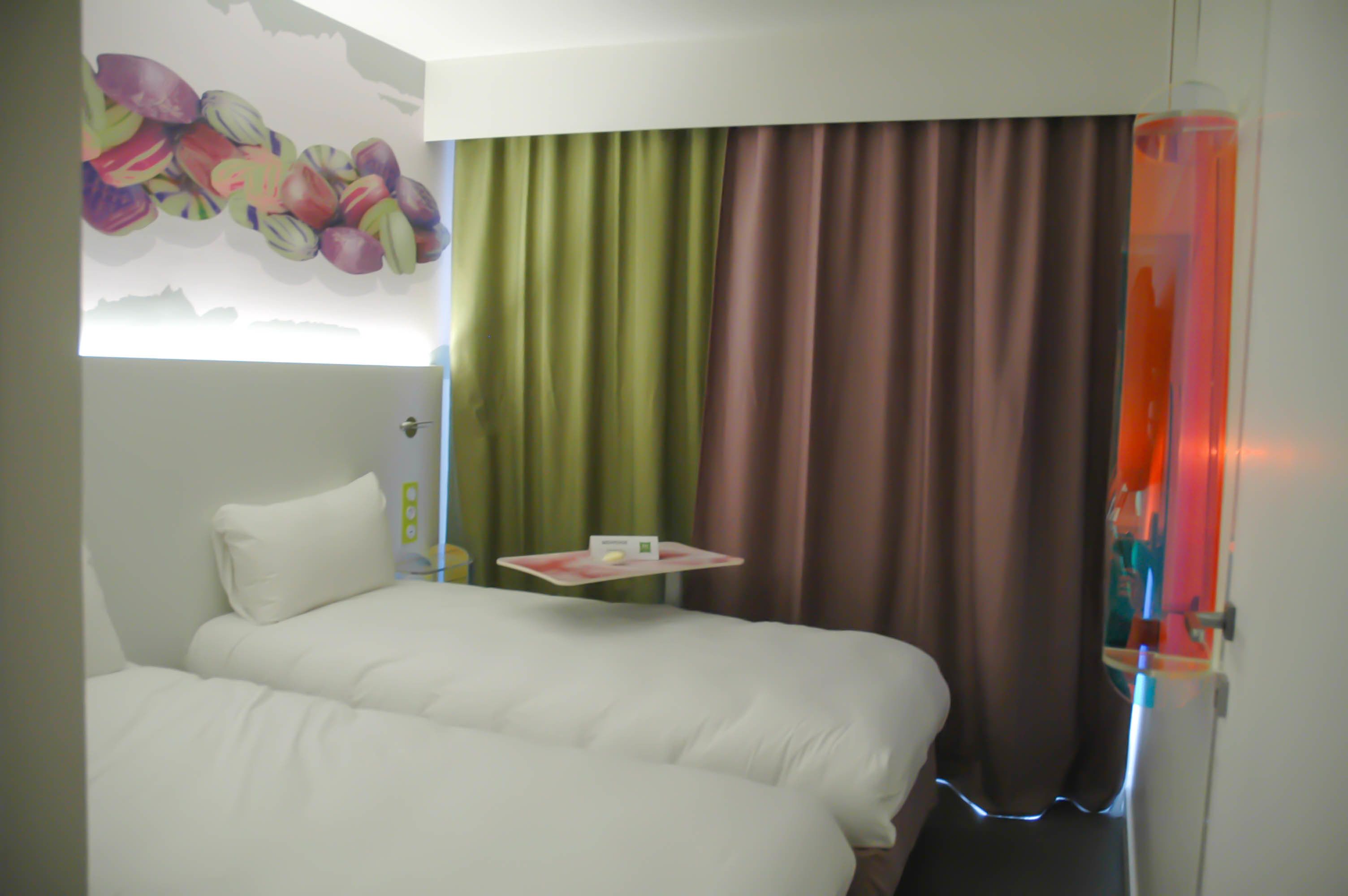 A hotel room with a bed, a small table with a tray, and a colorful mural on the wall.