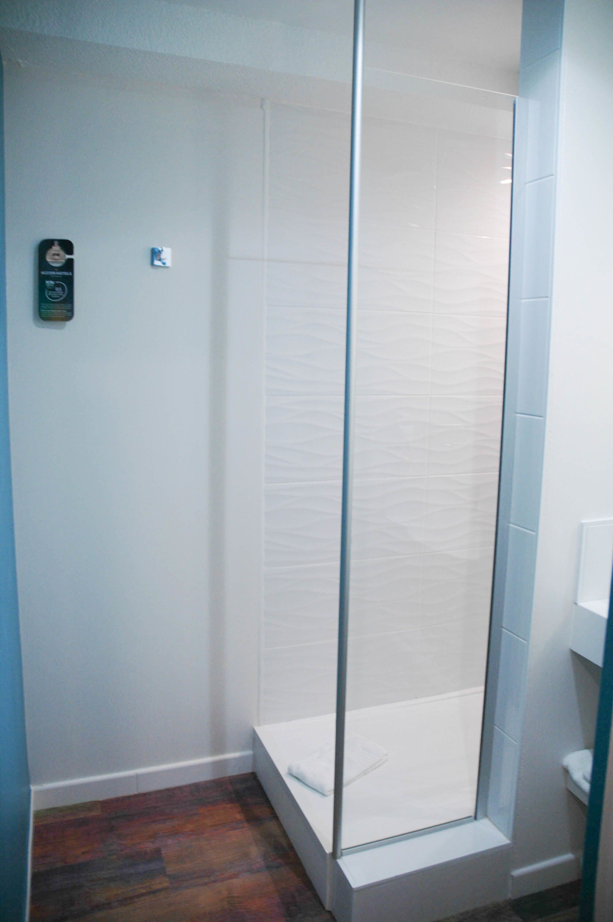 Una ducha con cerramiento de vidrio, pared de azulejos blancos y suelo de madera.