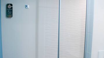 Una ducha con cerramiento de vidrio, pared de azulejos blancos y suelo de madera.