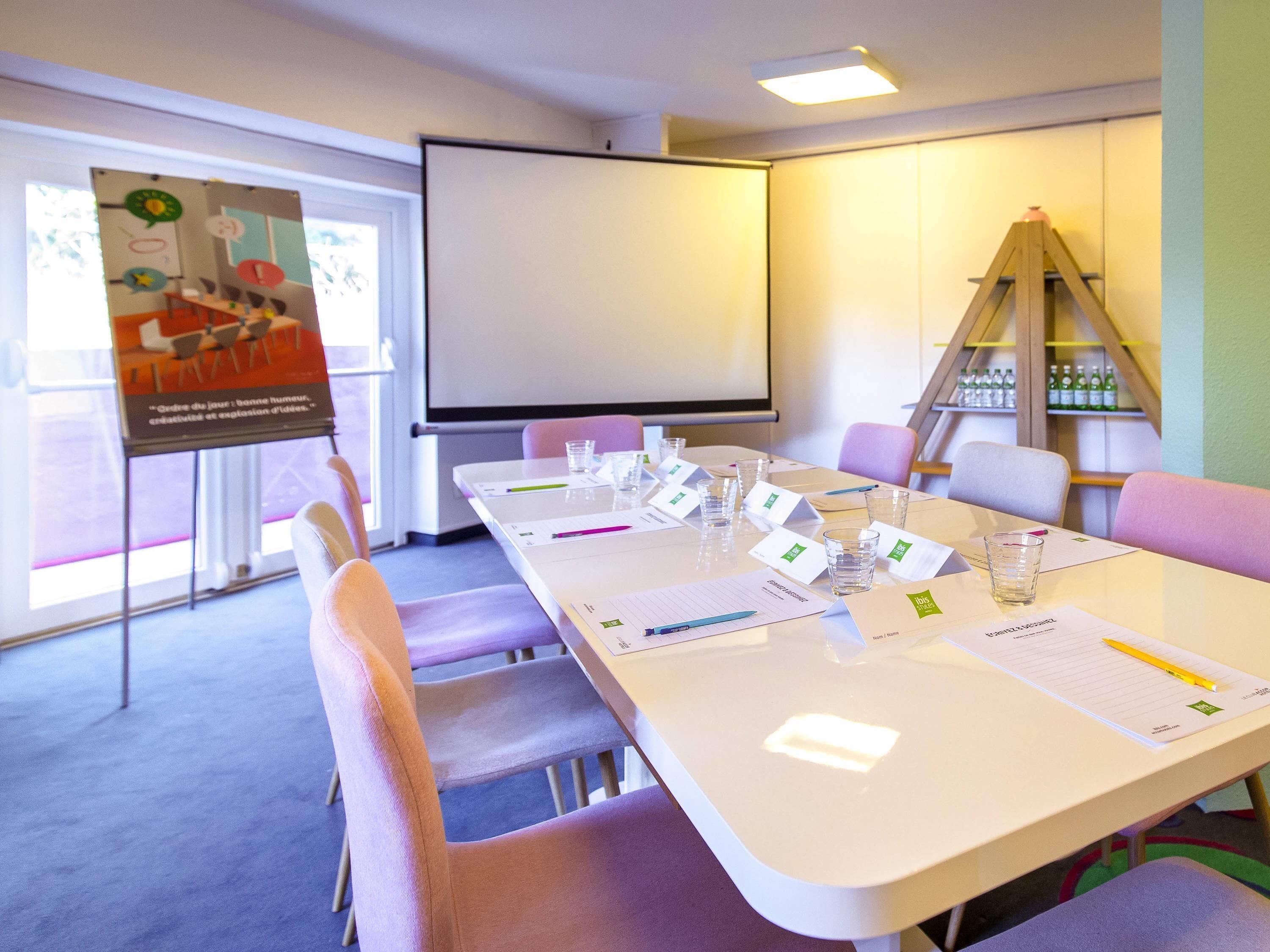Ett konferensrum med ett långt bord, stolar, en projektorduk och en affisch på väggen.