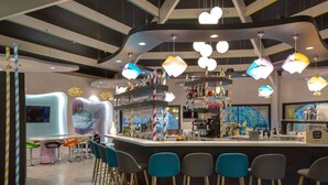 Un espace bar moderne avec une table de baby-foot, des tabourets de bar et une variété de bouteilles et de verres exposés sur des étagères.