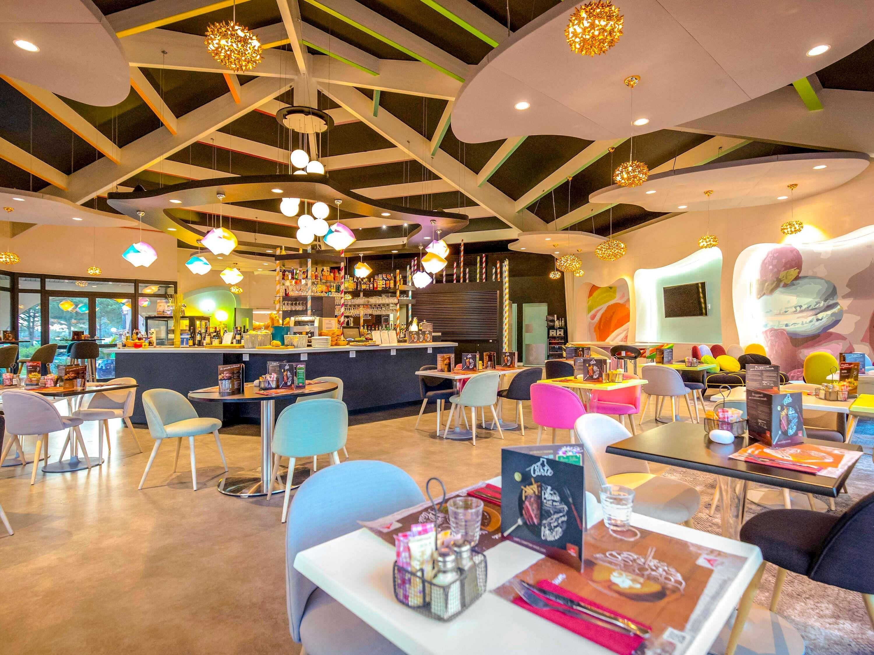 Un intérieur de restaurant moderne avec un bar, des chaises colorées et des luminaires sphériques suspendus.