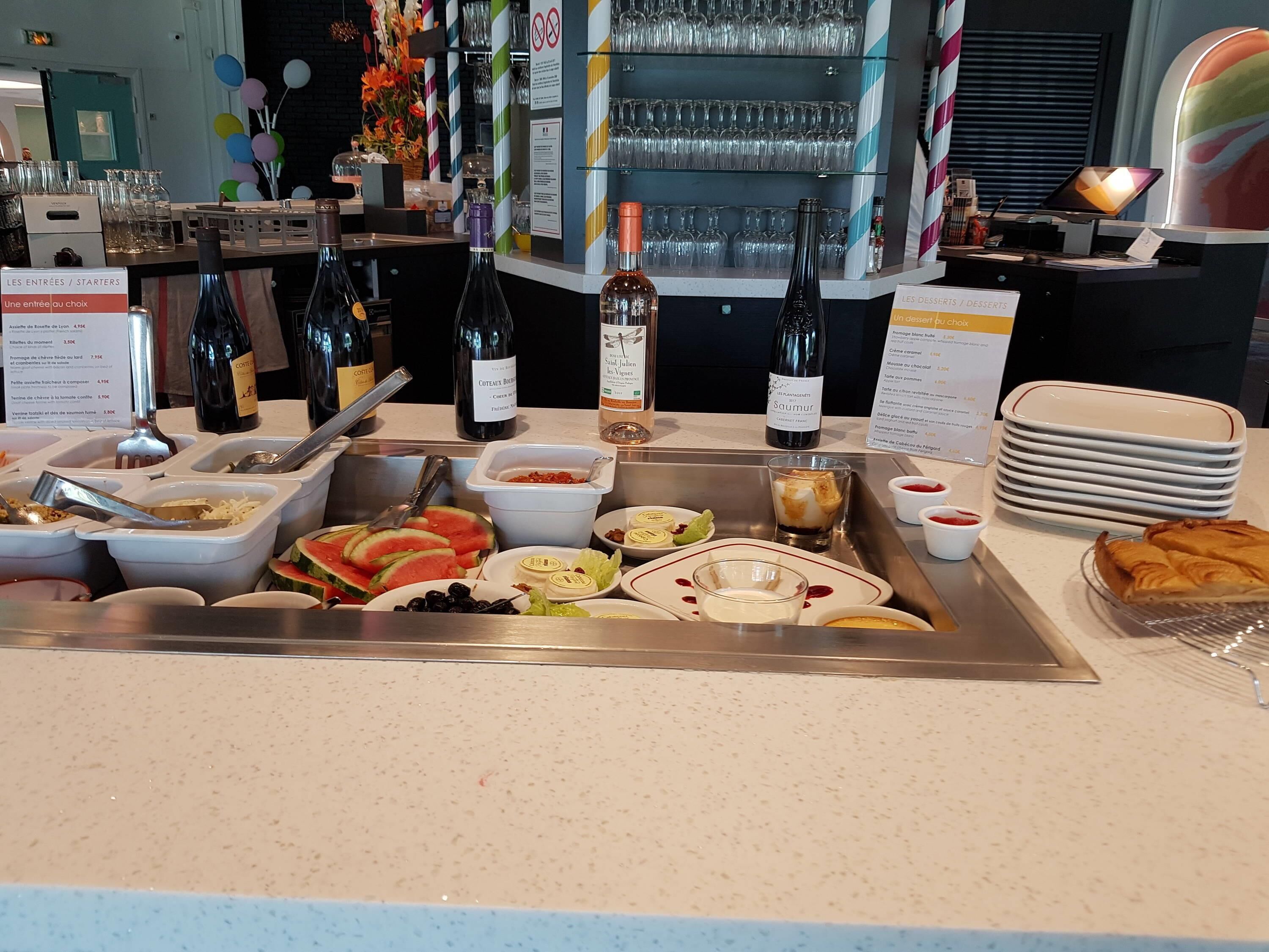 Un bufé con diversos alimentos, botellas de vino y una selección de vasos.