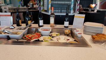Un bufé con diversos alimentos, botellas de vino y una selección de vasos.