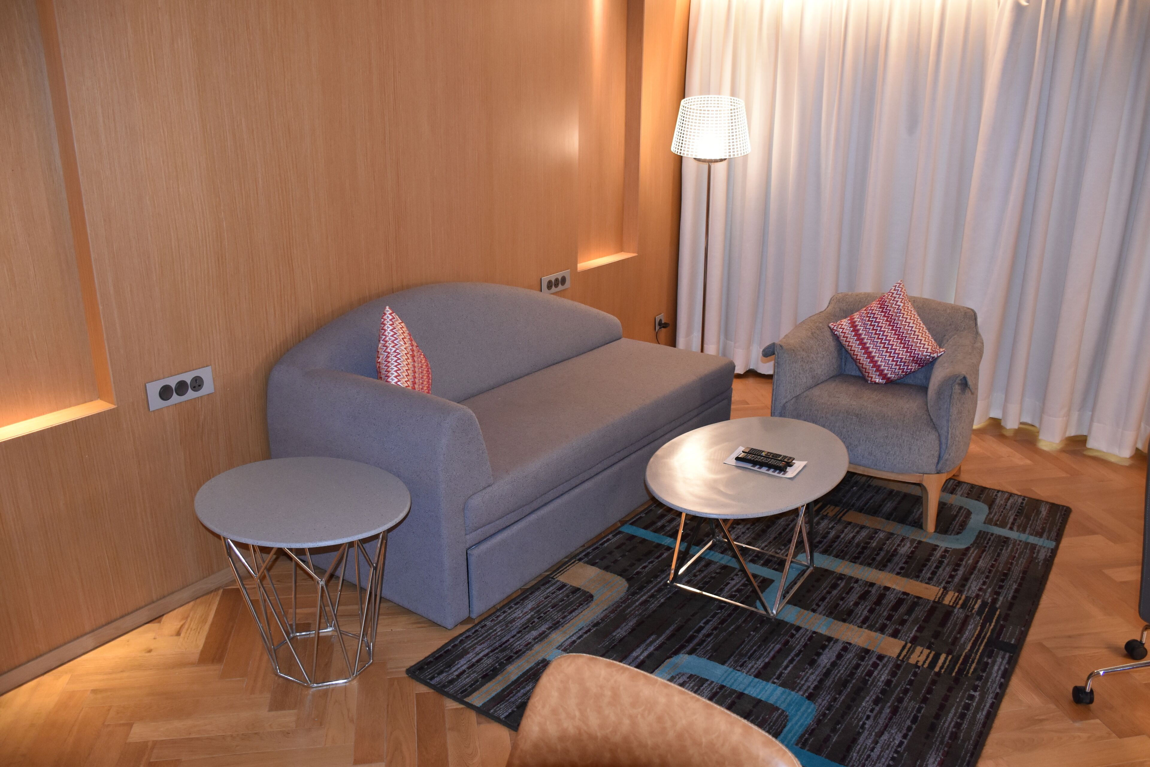 A modern room with a grey sofa, a small round table, a grey armchair, and a patterned rug.