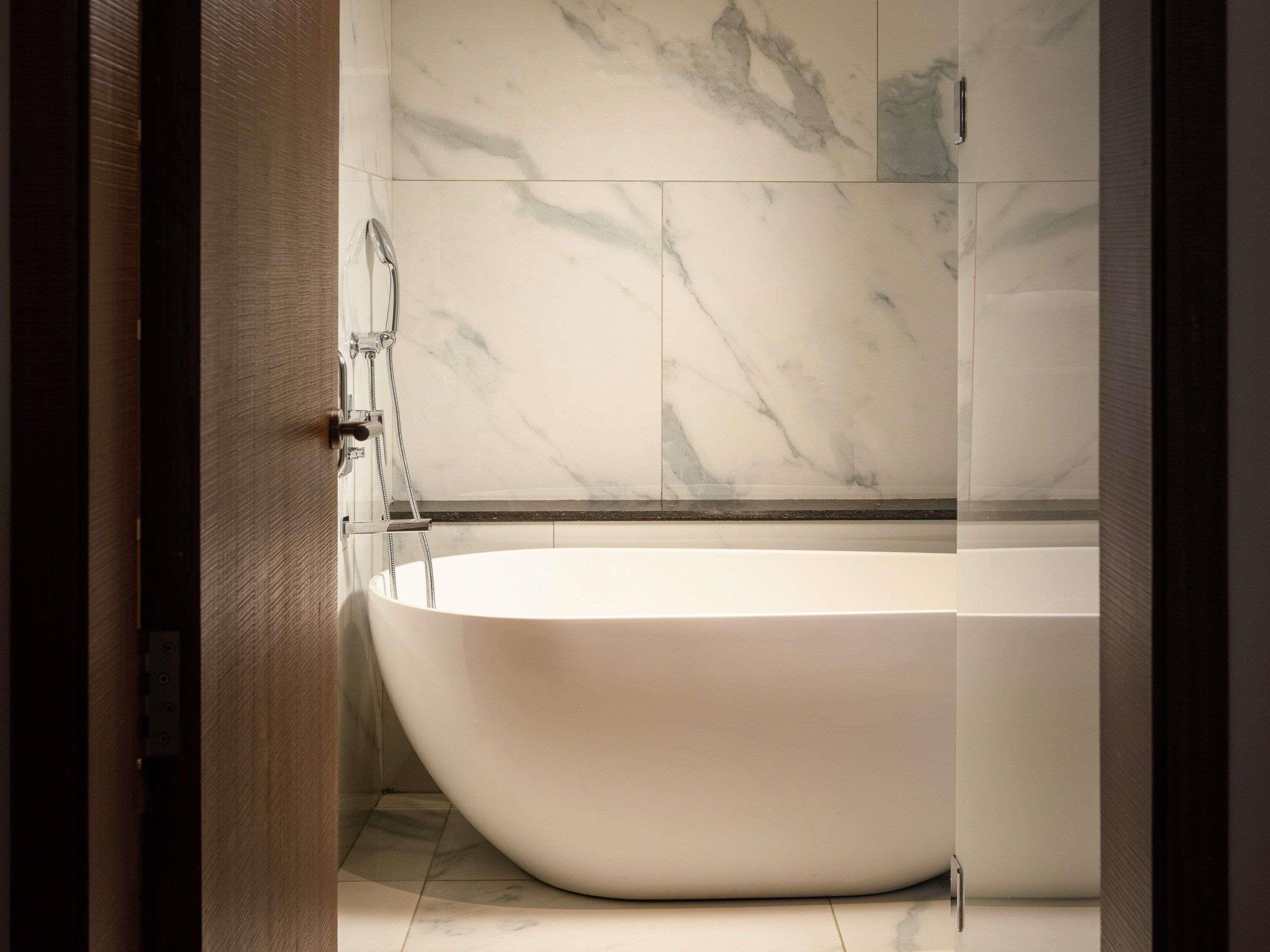 Une salle de bain moderne avec une baignoire sur pieds, des murs en marbre et une cabine de douche en verre.