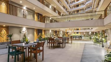 A multi-level hotel lobby with glass railings, dining tables, chairs, and potted plants.