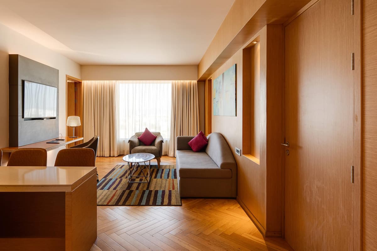 Een moderne hotelkamer met een flatscreen televisie, een bank, een stoel, een klein tafeltje en een tapijt met een herringbone patroon.