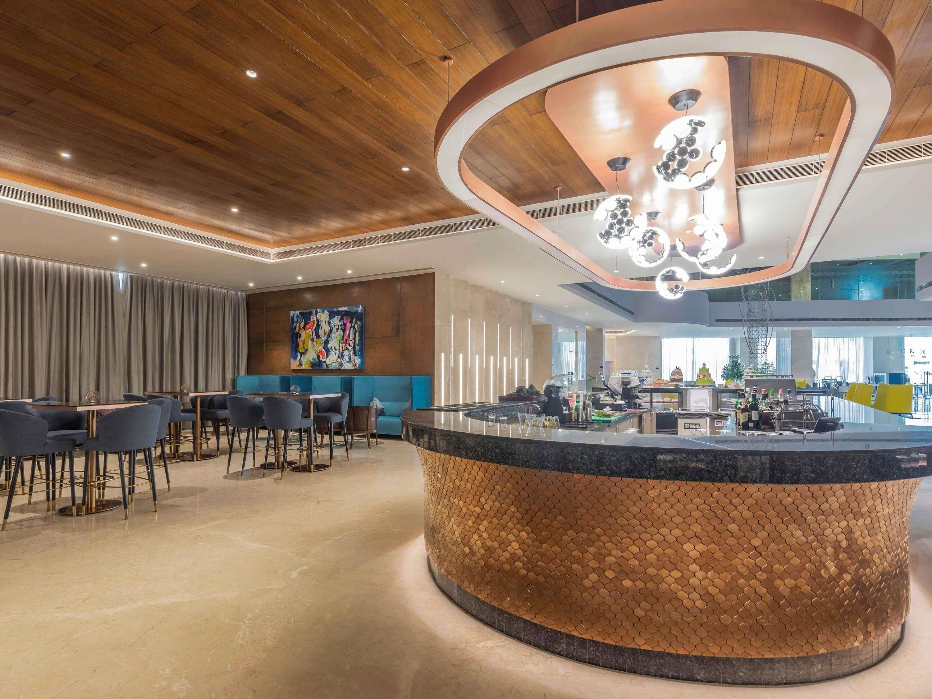 A modern hotel lobby with a central bar area, seating arrangements, and a large abstract painting on the wall.