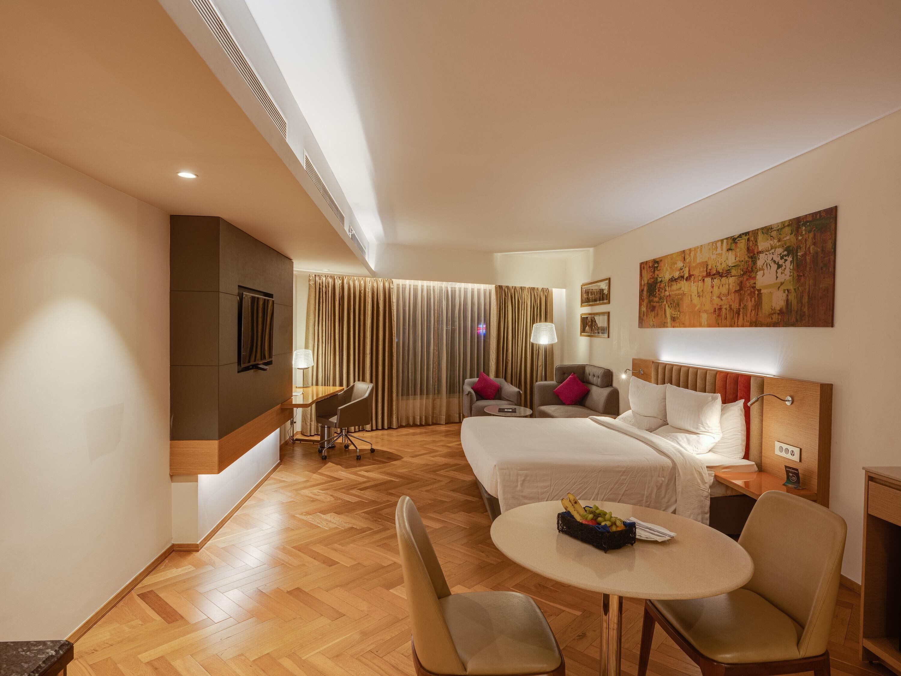 A hotel room with a bed, a desk, a chair, a table, and a painting on the wall.