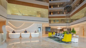 Een moderne hotellobby met een receptiebalie, een zithoek en een decoratief beeldhouwwerk.