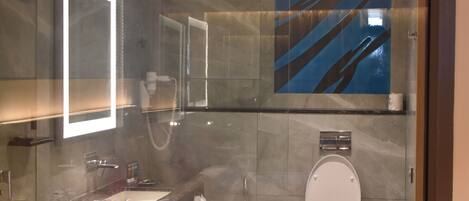 Une salle de bain moderne avec une cloison en verre, des toilettes blanches, un lavabo et un miroir.