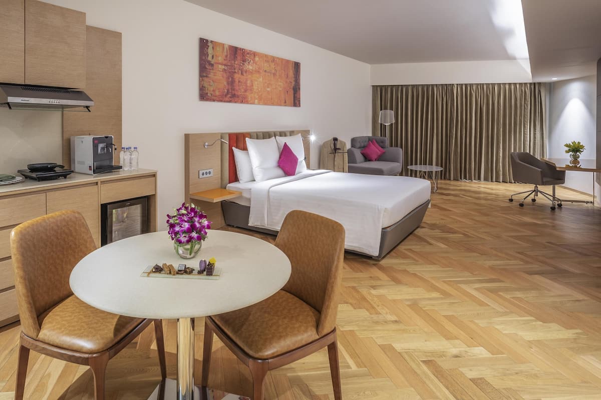 Een hotelkamer met een bed, een bureau, een stoel, een klein tafeltje met een bloevas en een kitchenette.