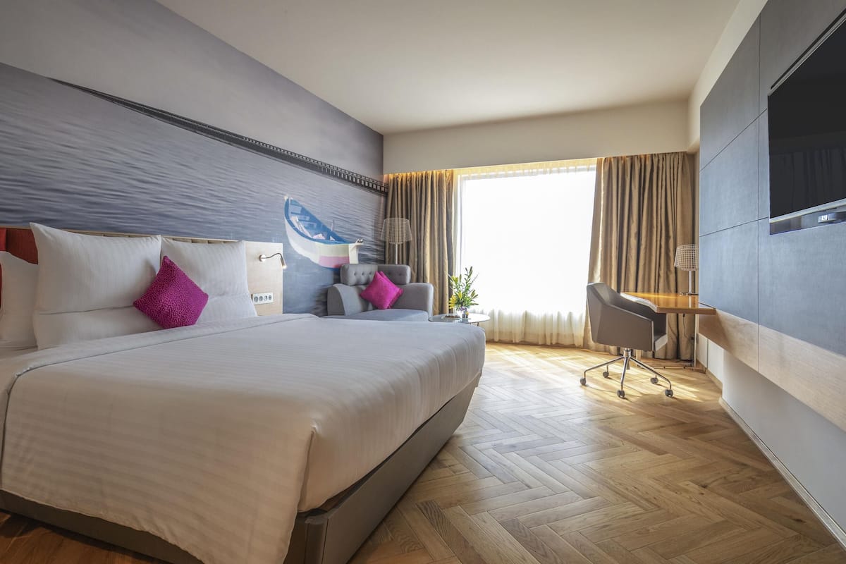 Een moderne hotelkamer met een groot bed, een bureau, een stoel, een televisie en een raam met gordijnen.