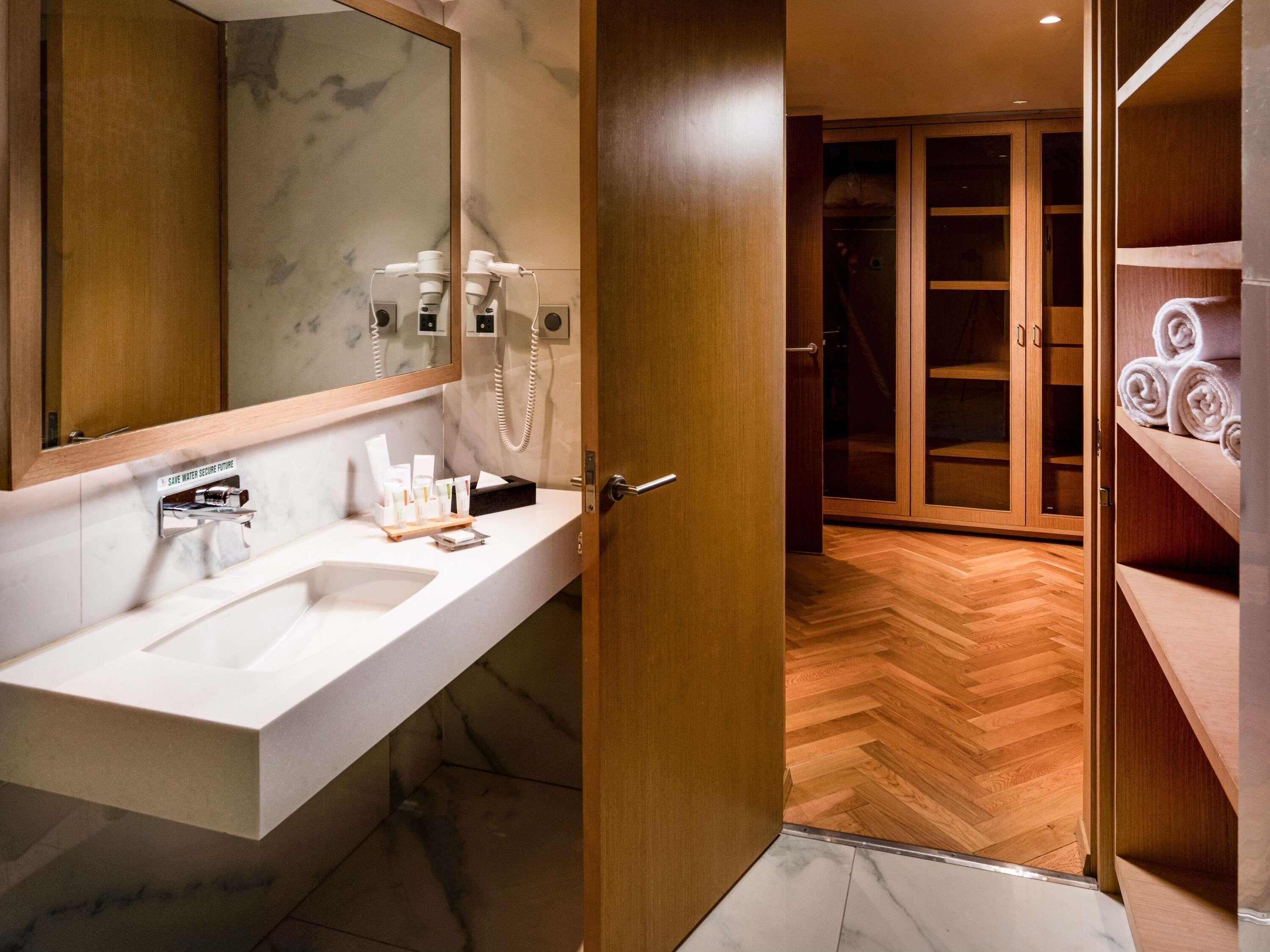 Un baño moderno con lavamanos de mármol, un espejo, un perchero para toallas y un mueble de tocador de madera.