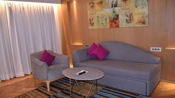 Una sala de estar moderna con un sofá gris, un sillón gris con un cojín rosa, una mesita redonda y un tapete colorido a rayas.
