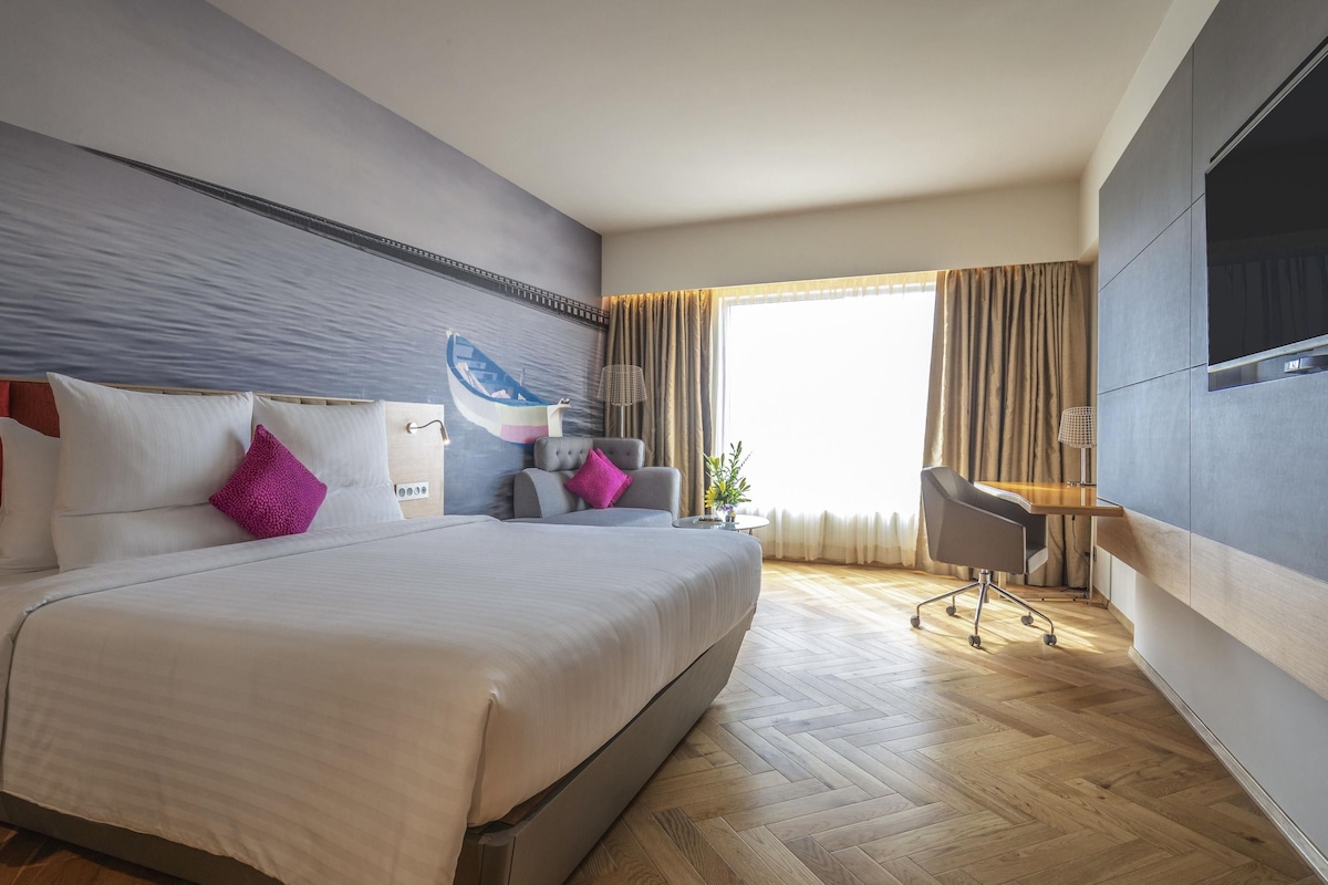 Une chambre d’hôtel moderne équipée d’un grand lit, d’un bureau, d’une chaise, d’une télévision et d’une fenêtre avec des rideaux.