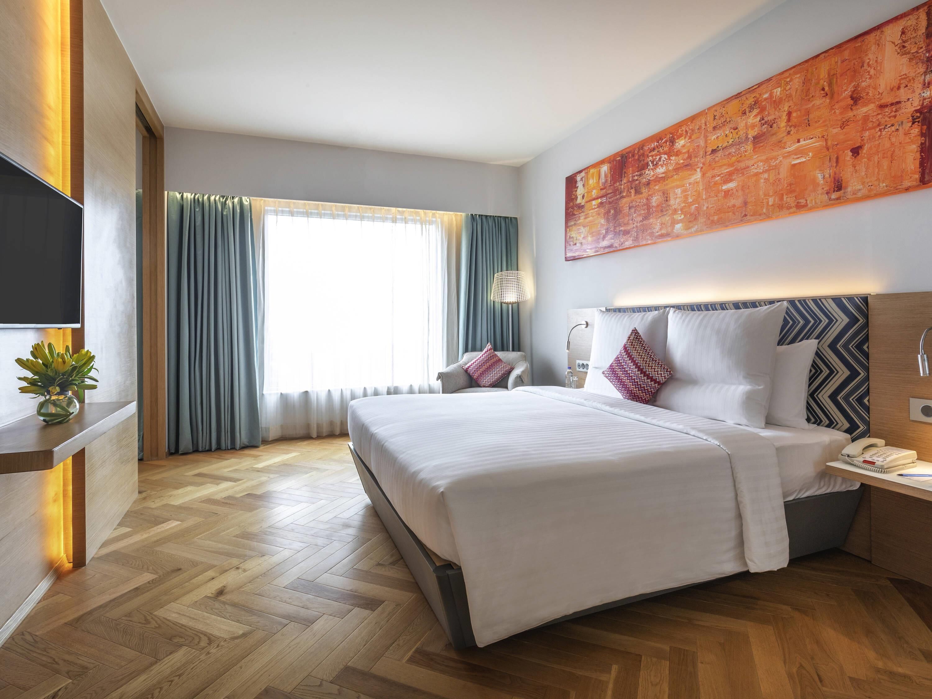 Ein Hotelzimmer mit einem großen Bett, einem Schreibtisch mit Telefon, einem Fernseher und einem Gemälde an der Wand.