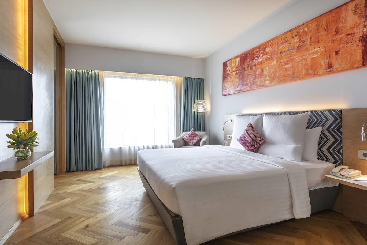 Een hotelkamer met een groot bed, een bureau met telefoon, een televisie en een schilderij aan de muur.