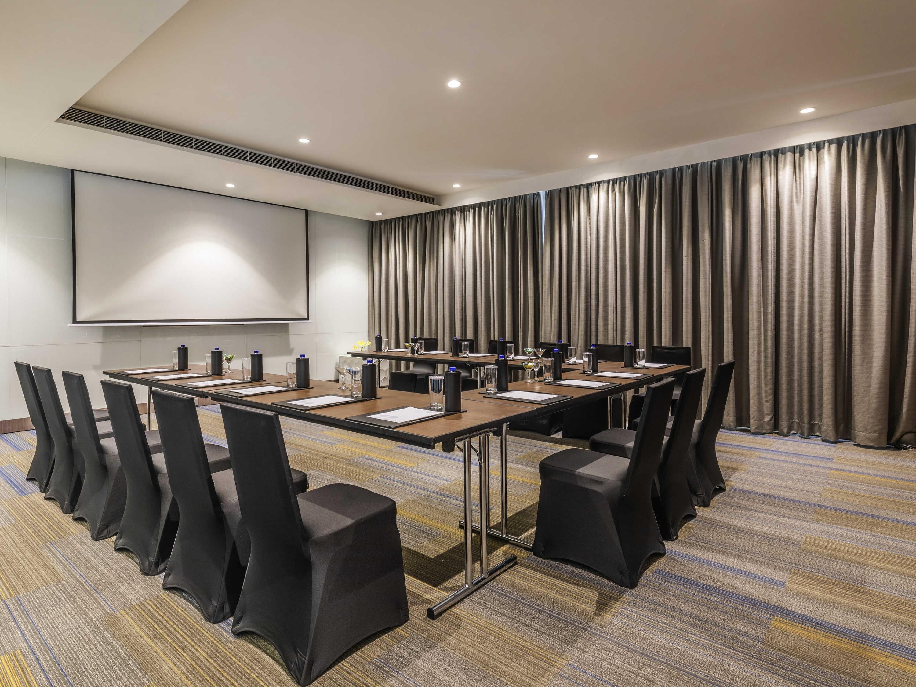 A conference room with a long table, chairs, a projector screen, and a large curtain.