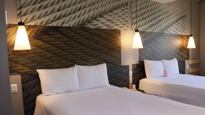A hotel room with two beds, each with white bedding and pillows, and a textured wall behind. There are two pendant lights hanging above each bed.