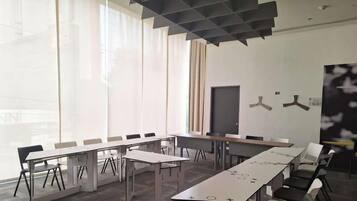 A conference room with a long table, chairs, a blackboard, and a large window with sheer curtains.