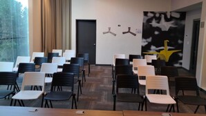 Une salle de conférence avec des rangées de chaises, une porte et un mur orné de deux ventilateurs de plafond et d’une grande œuvre d’art abstraite.