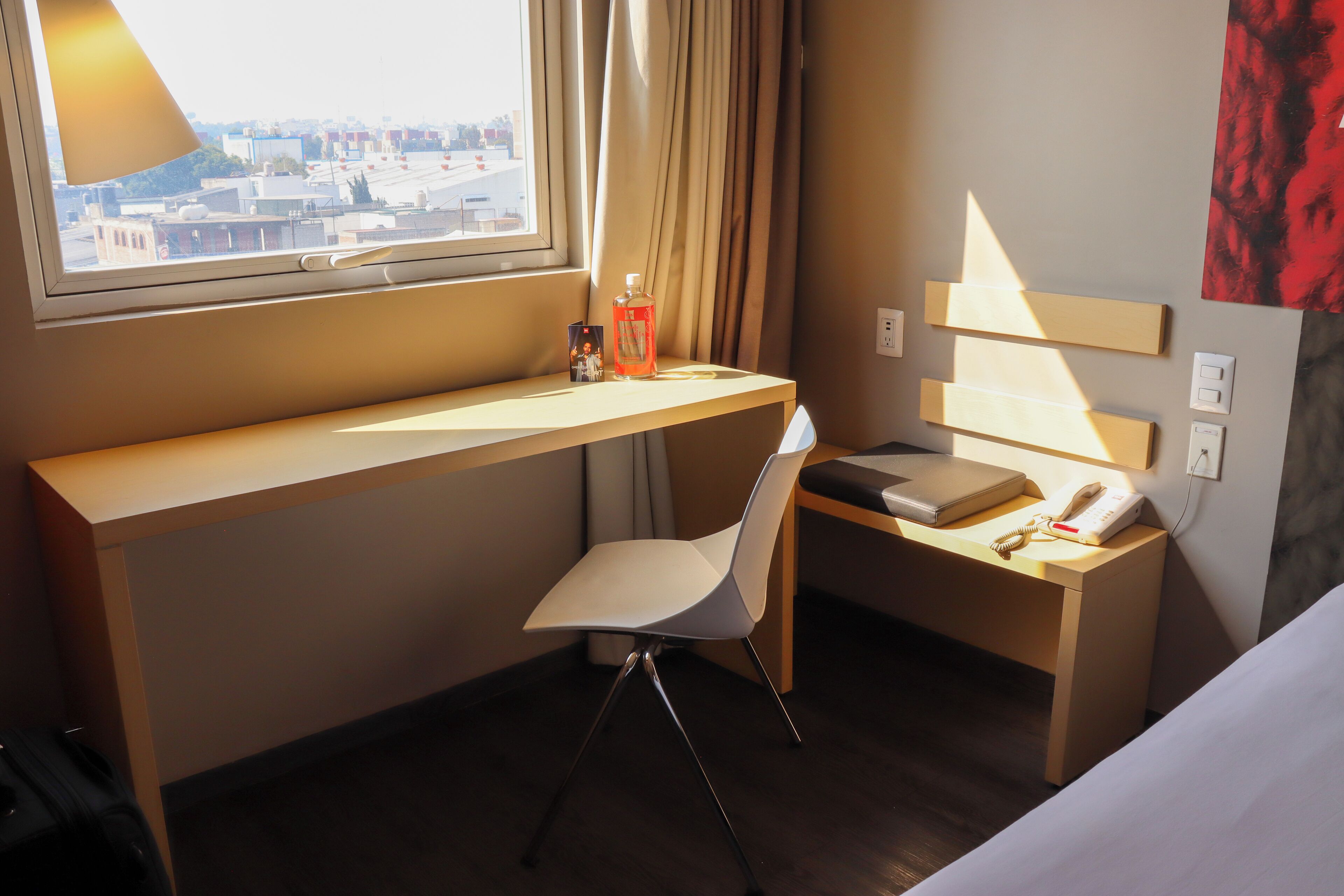A hotel room with a desk, chair, bed, and a window with a city view.