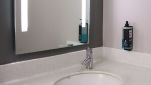 Een badkamer met een grote spiegel, een witte wastafel en een handzeepflacon aan de muur.