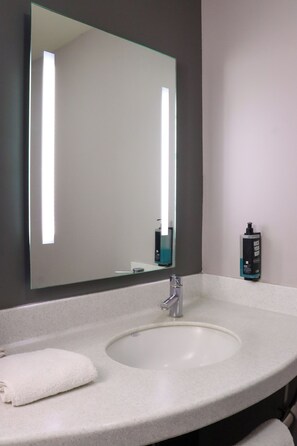 A bathroom with a large mirror, a white sink, and a bottle of hand soap on the wall.