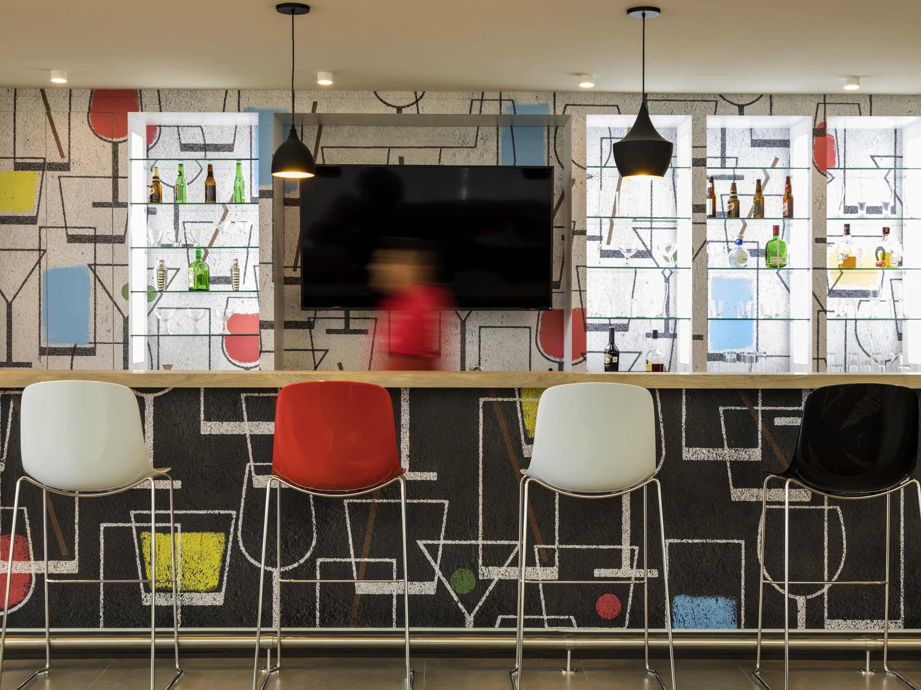 Zona de bar con diseño moderno, que incluye un televisor de pantalla plana grande, estantes de vidrio con botellas y un muro con diseño geométrico.