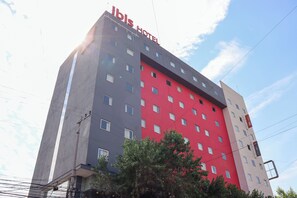 A multi-story hotel with a red and grey facade, multiple windows, and a visible sign reading "Ibis Hotel".
