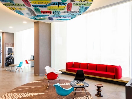 A modern lobby with a red sofa, colorful chairs, a round table, and a ceiling with various words and phrases.. ibis Mexico Tlalnepantla