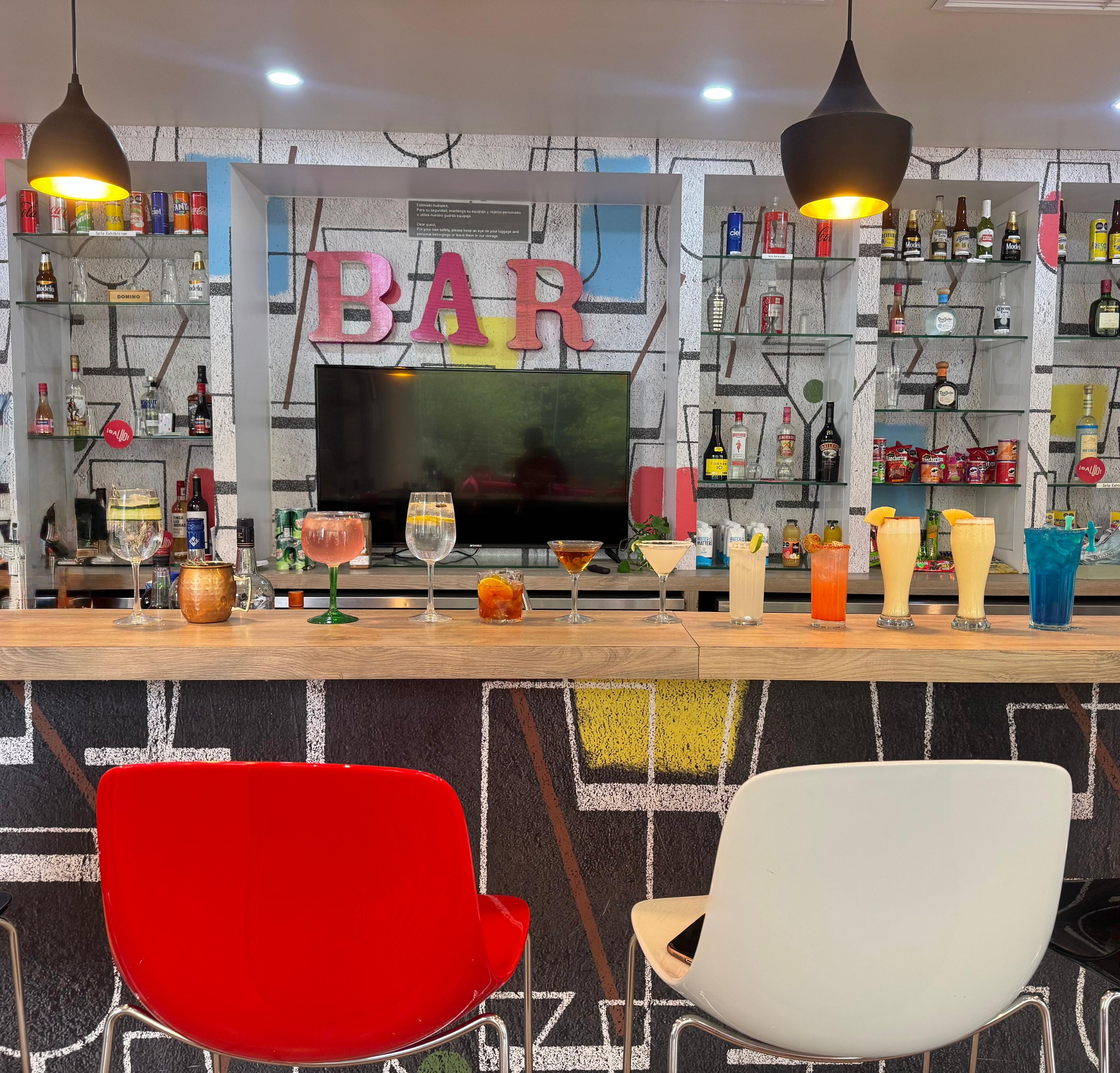 Un espacio de bar con un televisor, estantes con bebidas y dos sillones.