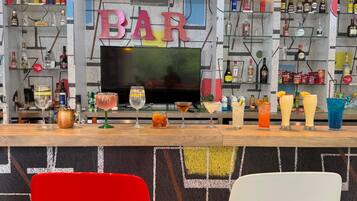 Un espacio de bar con un televisor, estantes con bebidas y dos sillones.