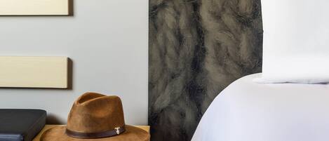 Una habitación de hotel con una cama, una mesita de noche, un sombrero y un cuadro en la pared.