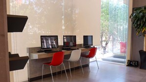 Un espace de bureau moderne comprenant trois bureaux, chacun équipé d’un écran d’ordinateur, et deux chaises, une rouge et une blanche.