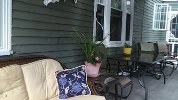 Een overdekt terras met een rieten bank, een eettafel en stoelen.