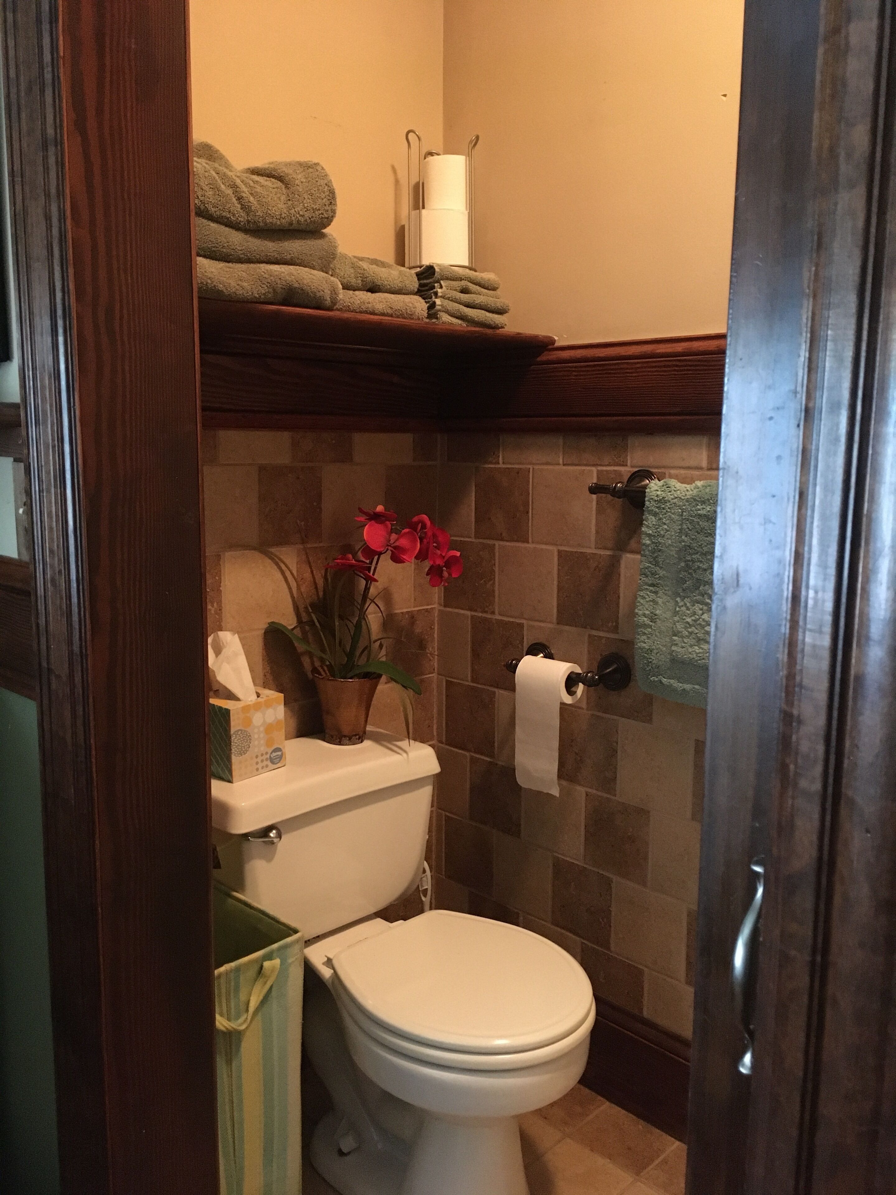 A bathroom with a toilet, a towel rack, a shelf with towels, a toilet paper holder, and a potted plant.